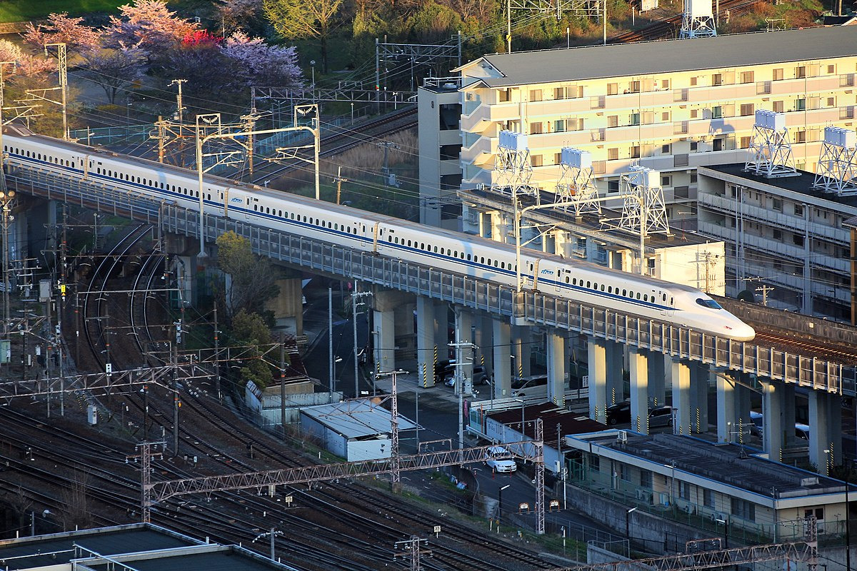 shinkansen train on an elevated track passing apartment buildings and cherry blossoms{width=200}